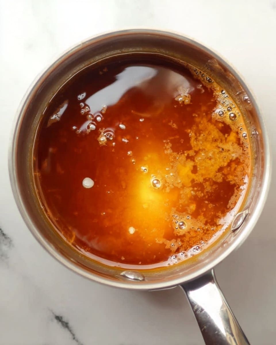The image shows four clear glass dessert cups, each with two layers: the bottom layer is smooth and light brown, resembling caramel or pudding, and the top layer is a slightly lighter, creamy brown liquid. On top of each cup is a small dollop of white whipped cream, sprinkled with chopped walnuts. The cups sit on a round silver tray, which is on a white marbled surface. Two silver spoons rest on the tray near the front of the image. The photo has a soft focus on the background cups and sharp focus on the front cup. photo taken with an iphone --ar 4:5 --v 7