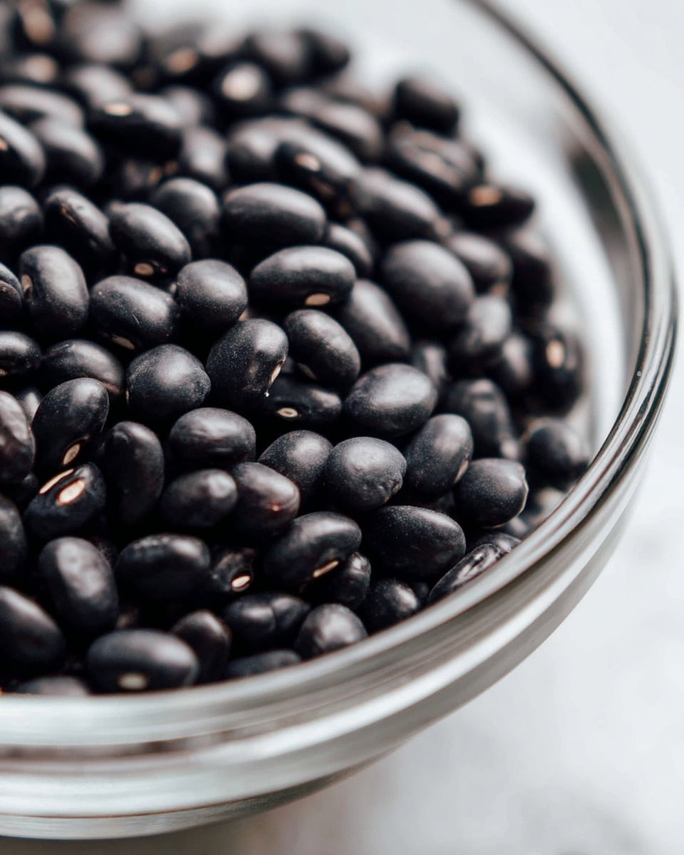 A close-up image showing fresh green beans inside a metal strainer. The green beans are bright green and whole, filling the strainer which has a mesh texture and two handles on opposite sides. The strainer sits on a white marbled surface with a small wet spot underneath, suggesting the beans were recently rinsed. The image is bright and focused on the green beans, with a clean, simple background. Photo taken with an iphone --ar 4:5 --v 7