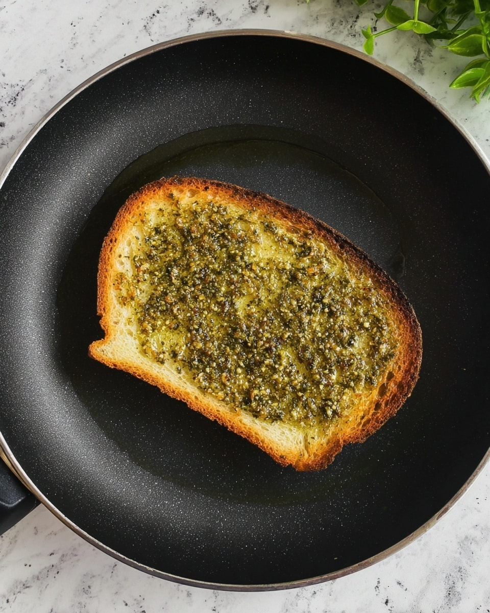 A single slice of toasted bread lies in the center of a black pan, placed on a white marbled surface. The bread has a rough texture with crispy golden-brown edges and is spread with a green pesto layer evenly across the top. On top of the pesto are three thick slices of white mozzarella cheese, placed in a row from left to right, partially overlapping each other. The top left corner of the frame shows a blurred cluster of green basil leaves. Photo taken with an iphone --ar 4:5 --v 7