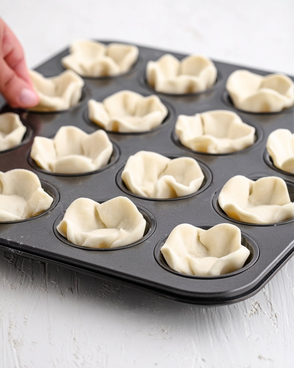 The first image shows a pan filled with chopped, cooked mushrooms mixed with small bits of orange vegetables, all in shades of brown and beige with a slightly soft texture. The second image shows a close-up of a metal muffin tray with several small dough cups that have white, slightly rough edges and are thinly spread inside each cup. A woman’s hand is holding a spoon with creamy, light beige filling that has green and brown bits, about to put it inside one of the dough cups. Both images have a background with a white marbled surface. photo taken with an iphone --ar 4:5 --v 7
