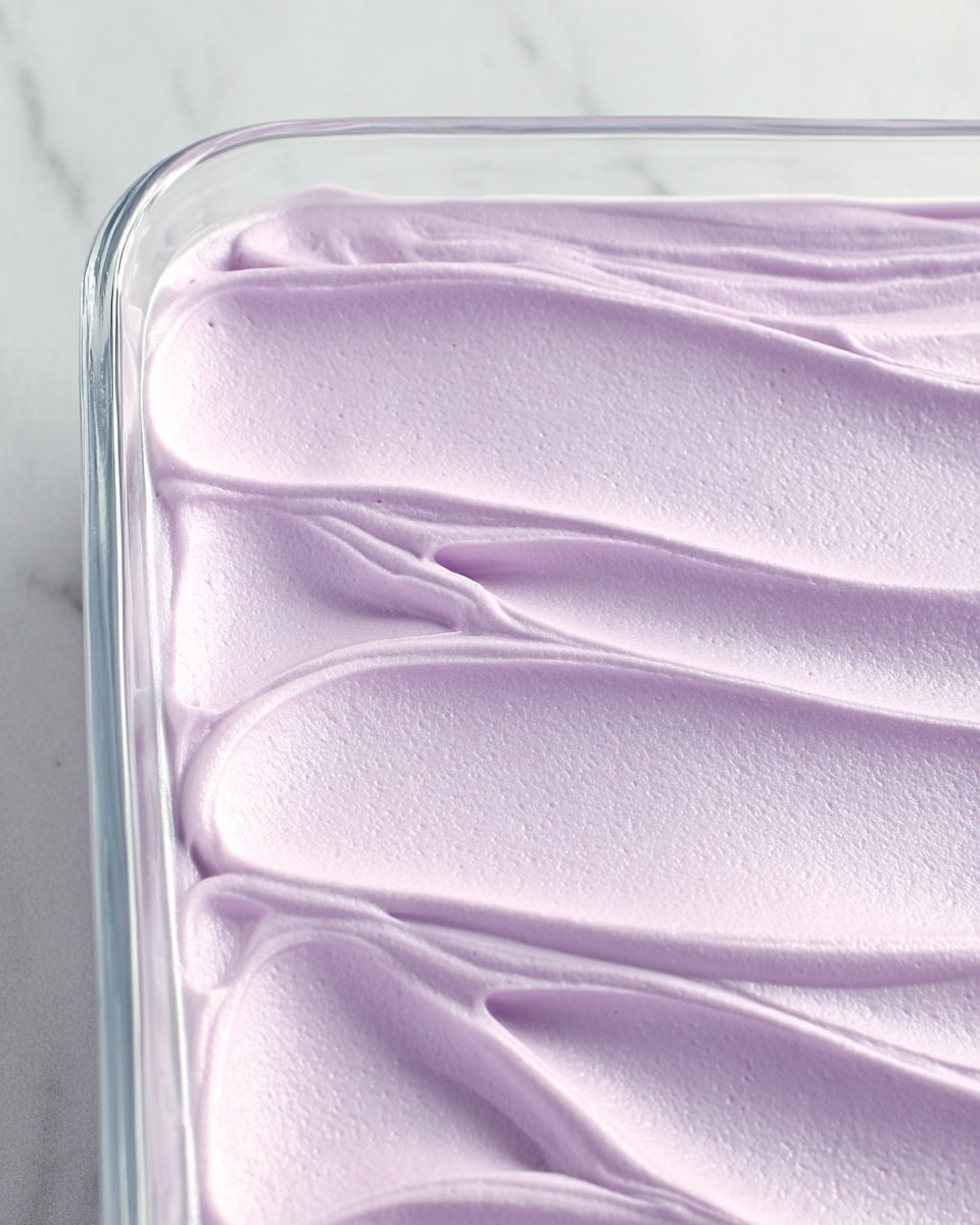 A square piece of purple cake with a soft, spongy texture sits on a white plate, topped with a thick layer of smooth, light purple frosting that drips slightly down the sides. A spoon holds a scoop of the cake, showing its moist inside and a bit of frosting clinging to both the cake piece and the spoon. The background is a white marbled surface. Photo taken with an iphone --ar 4:5 --v 7