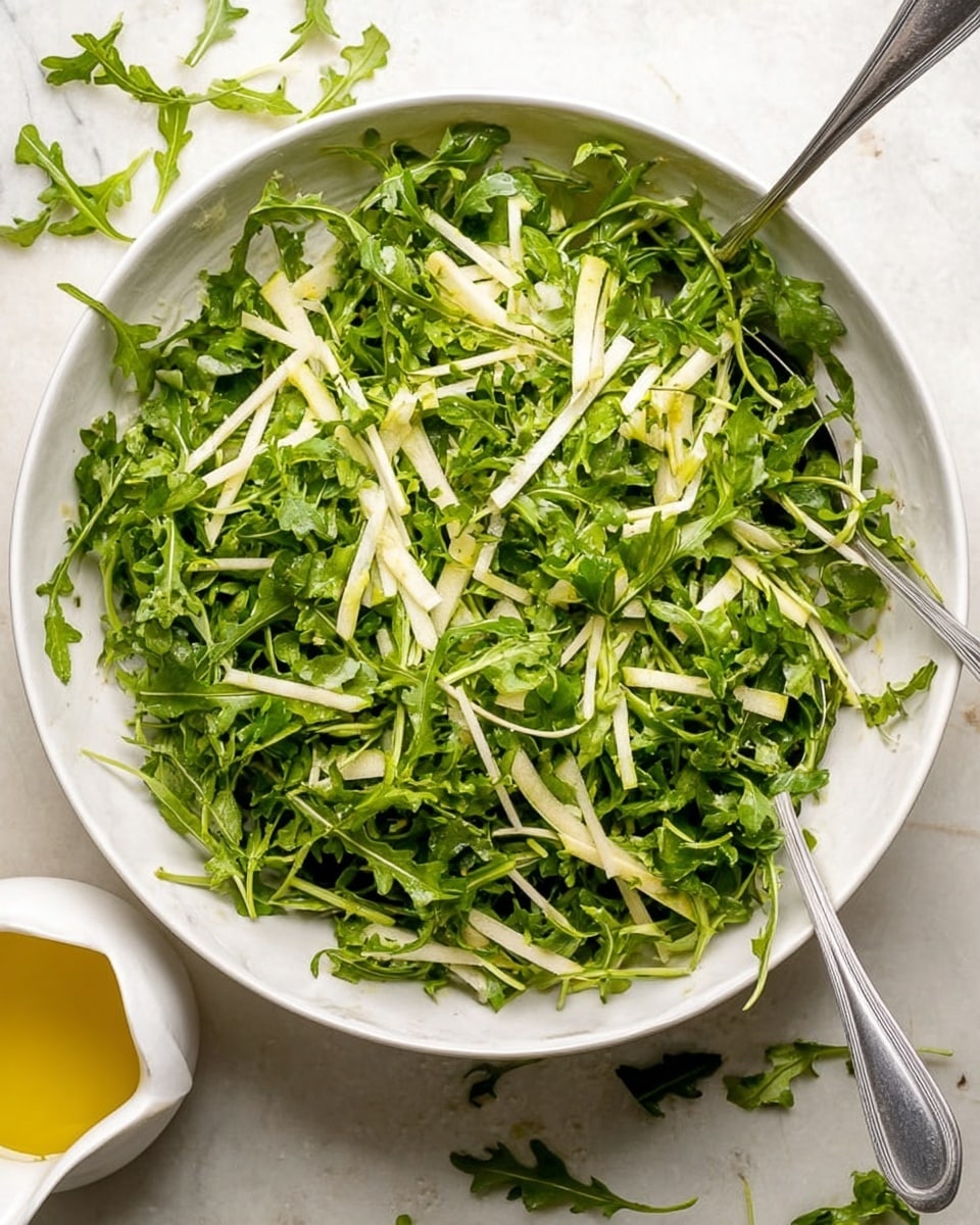A white bowl filled with two layers of fresh green arugula leaves with rough edges, mixed with thin white strips of peeled vegetable on top; a silver metal cup is pouring a smooth yellow dressing over the salad from above, with a woman's hand holding the cup. The bowl sits on a white marbled surface. Photo taken with an iphone --ar 4:5 --v 7