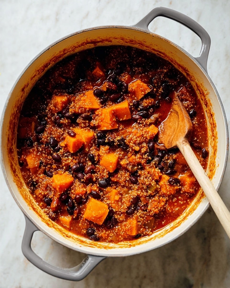 The image shows a large white pot filled with a thick stew that has three main visible layers: orange chunks of soft squash or sweet potato, black beans, and light tan quinoa grains, all mixed in a rich reddish-brown sauce. A wooden spoon with a square end rests inside the pot on the right side, partially covered in the stew. The pot has two gray handles on either side, and the stew's sauce has left an orange ring along the inside edge of the pot. The pot sits on a white marbled surface. photo taken with an iphone --ar 4:5 --v 7