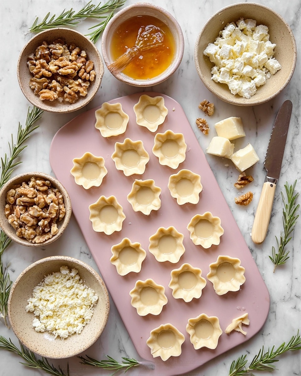 The image shows a pink mini muffin tray filled with small, raw tart shells made of light beige dough, each shell having four flared, petal-like corners and small fork holes on the base. Around the tray are four stone bowls: one with chopped walnuts, one with a golden-yellow egg wash and a brush, one with glossy amber jam with a small spoon, and one holding crumbled and solid white cheese alongside a small knife with a cream handle. The whole scene is set on a white marbled surface with sprigs of fresh rosemary on the sides. Photo taken with an iphone --ar 4:5 --v 7