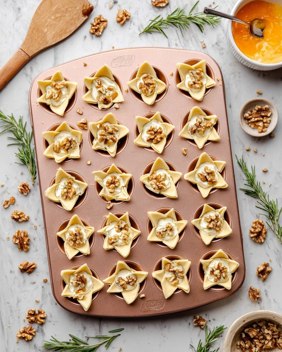 The image shows a rose gold muffin pan filled with 24 small pastry cups, each with four points of pale dough folded outward to form open star shapes, revealing a creamy white cheese filling topped with small pieces of light brown chopped walnuts. The muffin tray is placed on a white marbled surface with scattered walnut pieces and sprigs of fresh green rosemary around it. To the top right, a white bowl contains a small amount of orange spread with a silver spoon inside, and to the top left, a white bowl with some orange beaten egg and a wooden brush rest on the surface. The photo has a bright, natural light feel. photo taken with an iphone --ar 4:5 --v 7