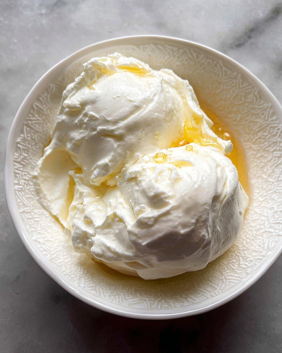 A white plate holds a single layer of creamy white cheese spread unevenly in a circular shape with a soft, fluffy texture, topped in the center by a cluster of whole, deep red cooked beets with a smooth and slightly shiny surface. The plate sits on a white marbled surface. photo taken with an iphone --ar 4:5 --v 7