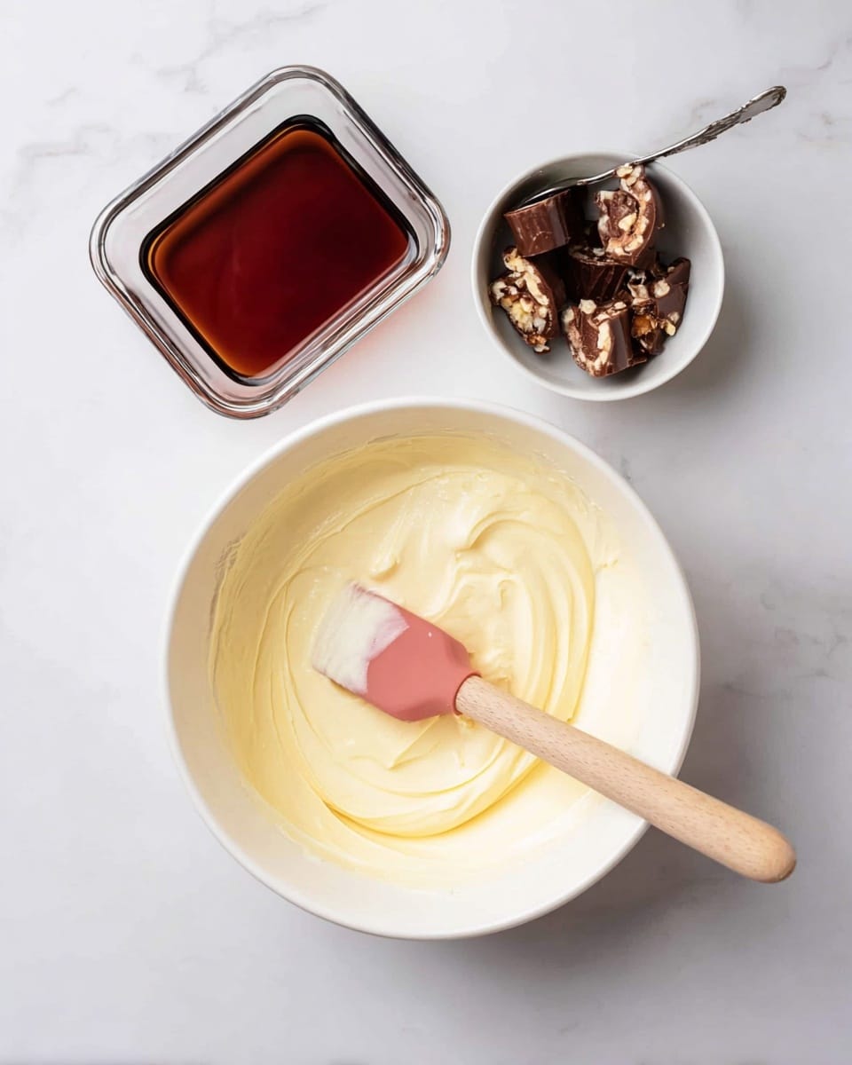 The image shows four clear glass cups with layered desserts on a white marbled surface. Each cup has three main layers: a bottom layer of light brown crumbs, a thick middle layer of creamy white filling, and a layer of small dark chocolate chunks mixed with more creamy white filling. On top of each dessert, there is a smooth layer of the creamy filling dusted with cocoa powder. Each cup is decorated with a halved round chocolate candy with a shiny dark center and lighter brown shell placed on top. One cup in the front has a silver spoon inside with some of the dessert stirred and scooped, showing the creamy texture mixed with the chocolate bits. There are some cocoa powder sprinkles and broken pieces of the round chocolate candy scattered on the surface. photo taken with an iphone --ar 4:5 --v 7