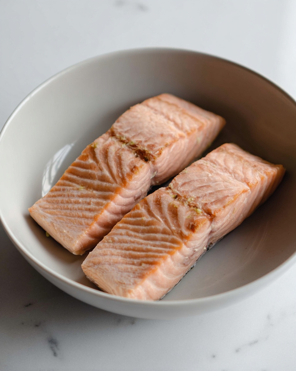 A white bowl holds three main layers of food: the bottom layer is light pink shredded salmon spread evenly around the bowl, the middle layer is bright orange diced salmon pieces piled in the center, and the top layer shows two dollops of thick white cream with fresh green dill scattered on and around the cream, with a few black pepper and lemon zest specks sprinkled over it, all set against a white marbled surface. photo taken with an iphone --ar 4:5 --v 7