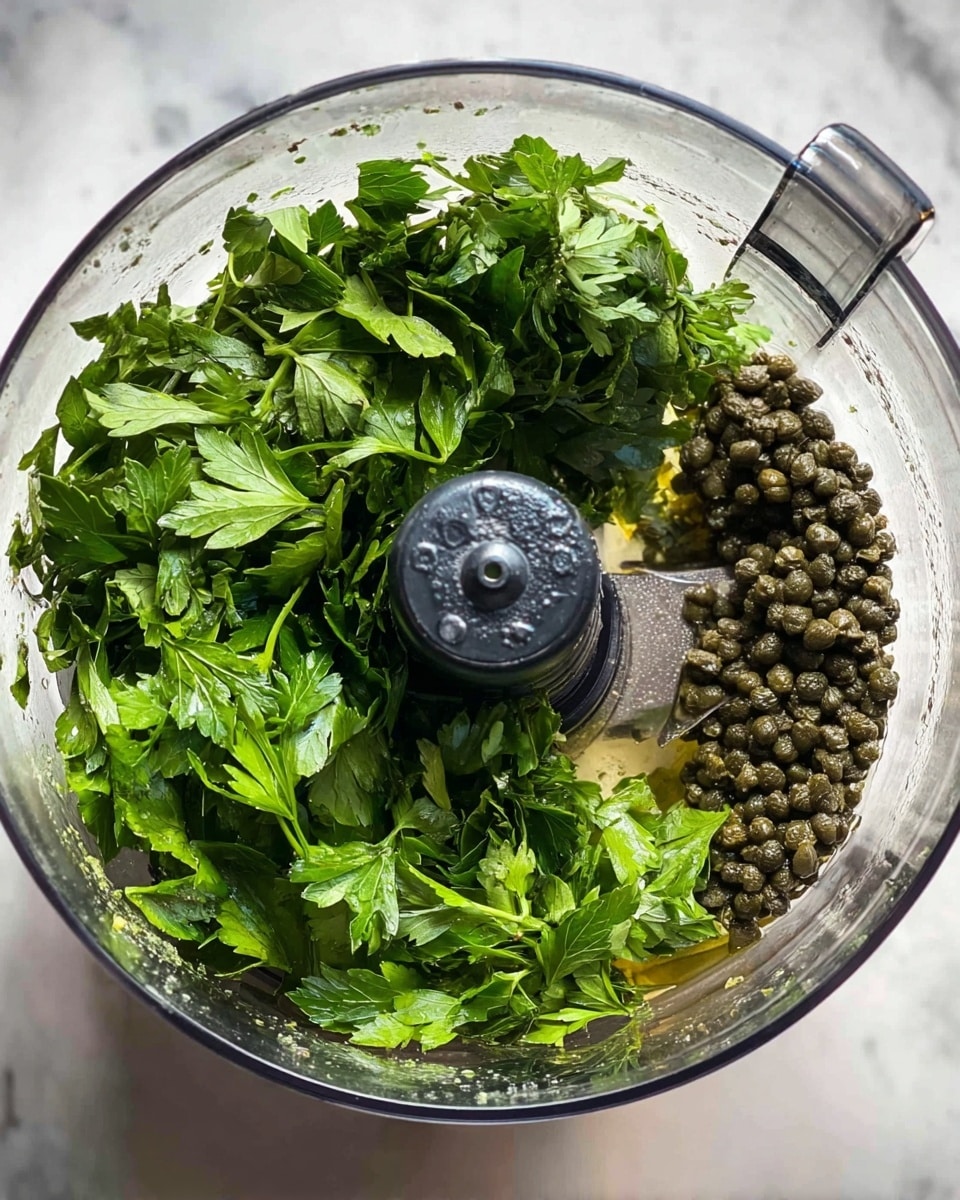 A close-up top view of a glass food processor bowl filled with bright green, slightly textured sauce with small bits spread across its surface. The sauce clings to the sides as well as pools at the base around the sharp silver blade with a dark gray center. The whole container is set on a white marbled surface. photo taken with an iphone --ar 4:5 --v 7