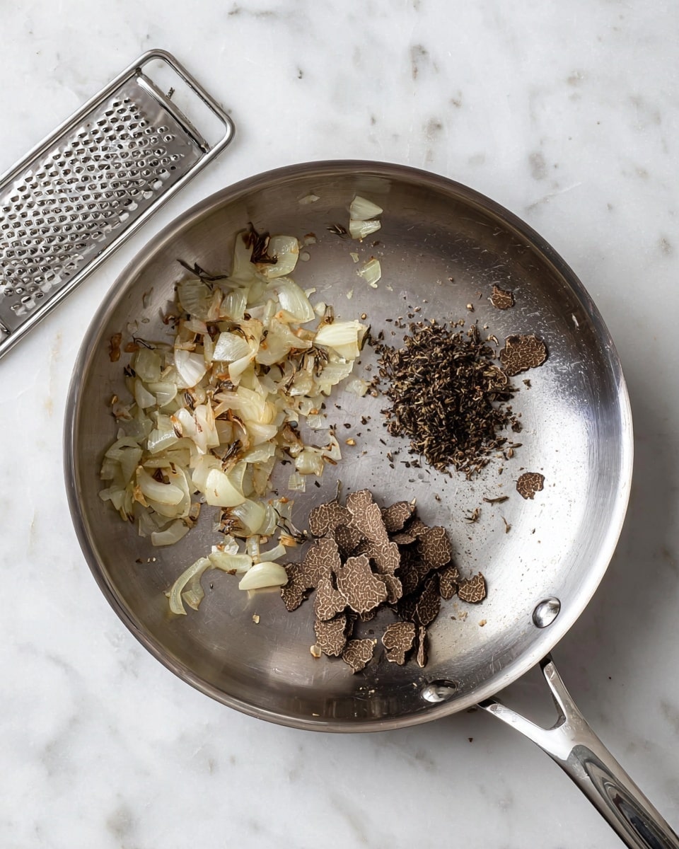 The image shows a top view of a metal pot filled with a creamy white sauce that has small flecks of herbs and spices scattered throughout. In the pot, a silver spoon with a decorative handle rests, partially dipped into the smooth sauce, showing a bit of its thick texture. The pot sits on a white marbled surface, and part of the pot handle with the brand name