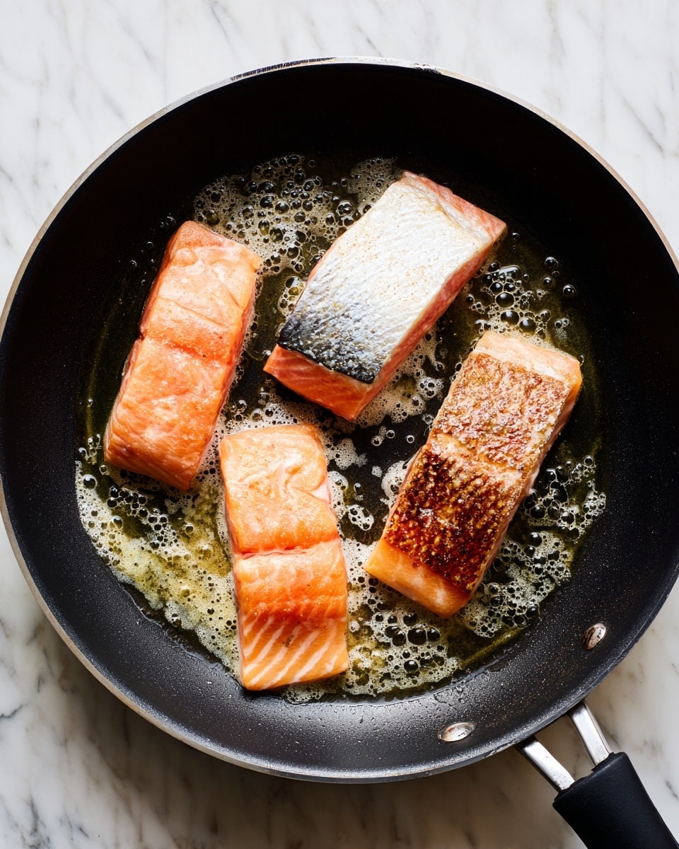 Four pieces of cooked fish fillets are placed side by side on a white marbled surface. Each fillet is rectangular with a slightly crispy, brownish-orange top layer that is coated evenly with dark brown and black spices and herbs. The fish texture under the spices appears moist and flaky, with small oil spots around the fillets. The lighting highlights the texture and seasoning details on the fish, making it look flavorful and well-prepared. photo taken with an iphone --ar 4:5 --v 7