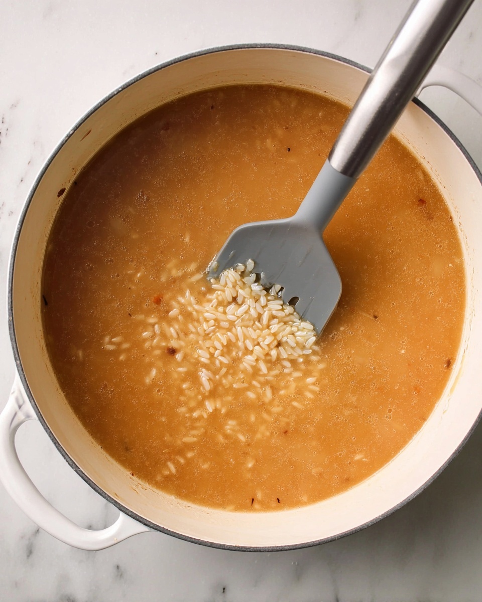 A large white pot filled with cooked orzo pasta in a light orange sauce, the pasta appearing soft and glossy with small black specks scattered throughout; a silver spoon is scooping some orzo from the pot, creating a slight depression in the middle of the mound; the pot sits on a surface with a white marbled texture, and the overall look is warm and inviting, showing the texture and shine of the pasta clearly photo taken with an iphone --ar 4:5 --v 7