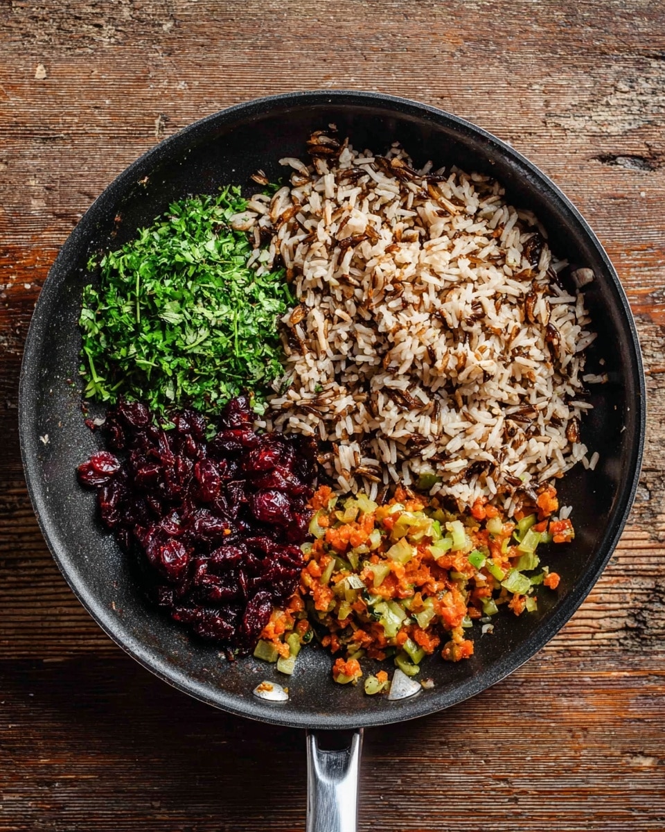 A black frying pan is placed on a wooden surface showing four different ingredients separated in sections inside the pan. The largest section holds a mix of cooked wild and brown rice in light brown with darker strands. To the left of the rice, there is a pile of finely chopped green herbs with a fresh leafy texture. Below the herbs, there are dark red dried cranberries with a shiny, slightly wrinkled look. To the right and below the berries, there are small diced cooked vegetables in orange and light green colors that look soft and slightly translucent. The pan handle is metal and shiny. Photo taken with an iphone --ar 4:5 --v 7