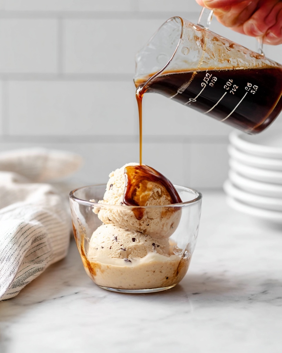 A close-up image shows a white plate on a white marbled surface with a scoop of light cream-colored ice cream mixed with small dark chocolate swirls, placed near the center of the plate. The ice cream appears smooth and creamy with soft texture variations. A metal ice cream scooper is touching the scoop, held by a woman's hand, capturing the ice cream shape with slight ridges and shiny highlights. The scene is bright with soft natural light highlighting the ice cream texture and the clean white plate photo taken with an iphone --ar 4:5 --v 7