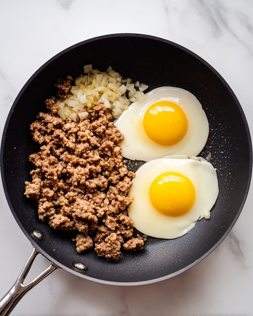 A black frying pan with two main parts inside: on the left side is a layer of cooked ground meat mixed with small white onion pieces, showing a rough, crumbly texture in brown and light yellow colors; on the right side are two raw eggs, each with bright yellow yolks and clear, shiny whites spreading out in irregular shapes, partially touching the meat; the pan sits on a white marbled surface photo taken with an iphone --ar 4:5 --v 7