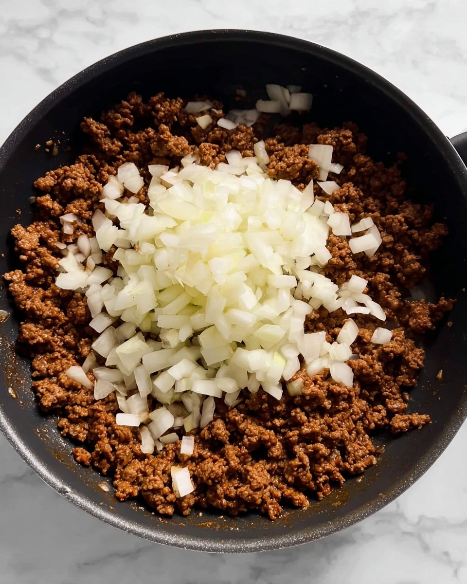 A black pan filled with cooked ground meat, which is brown and crumbly, forms the bottom layer. On top, there is a mound of freshly chopped onions that are white and slightly translucent, with some onion pieces spread lightly around the meat. The pan sits on a white marbled surface, with no other items visible in the frame. The overall look shows a step in cooking where the onions are just about to be mixed into the browned meat. photo taken with an iphone --ar 4:5 --v 7