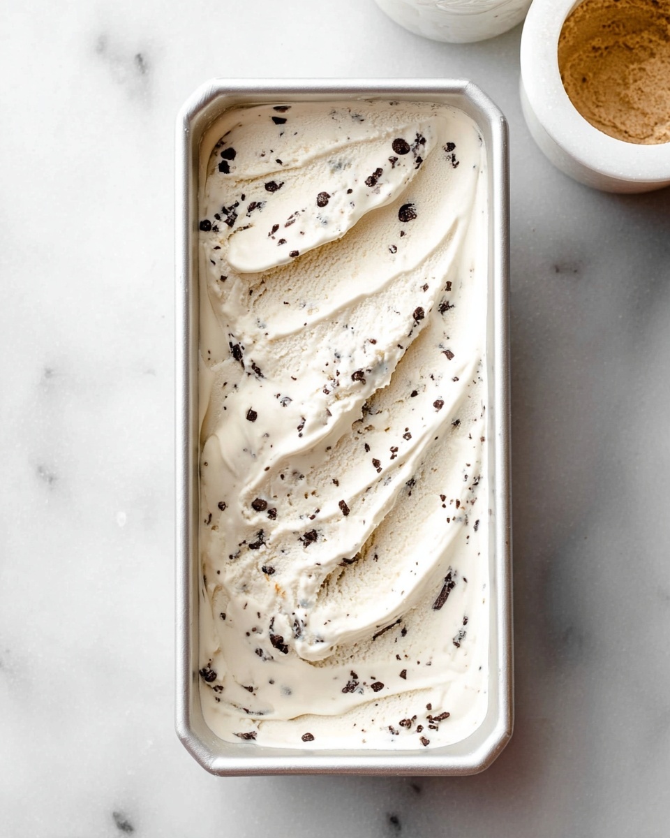 The image shows two scoops of light cream-colored ice cream with small dark chocolate pieces mixed inside and a few larger chocolate chunks sprinkled on top. The ice cream is in a white, speckled bowl with a textured vertical ridged pattern. In the background, there is a white rectangular container with more scoops of the same ice cream, and another white speckled bowl partially visible, filled with more ice cream. The surface beneath everything is a white marbled texture, and a silver spoon lies nearby on the surface. photo taken with an iphone --ar 4:5 --v 7