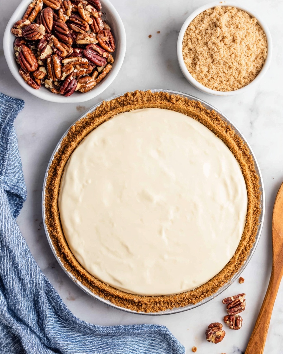 The image shows a round pie with two main layers. The bottom layer is a golden brown crust made with pecans, showing small pieces of nuts on the edge. The top layer is a smooth, creamy pale white filling spread evenly within the crust. Above the pie, there are two small white bowls: one filled with whole pecans that are brownish-red with wrinkled textures and the other filled with crumbly light brown sugar. The scene is set on a white marbled surface with a wooden spoon on the right and a blue and white striped cloth on the left photo taken with an iphone --ar 4:5 --v 7