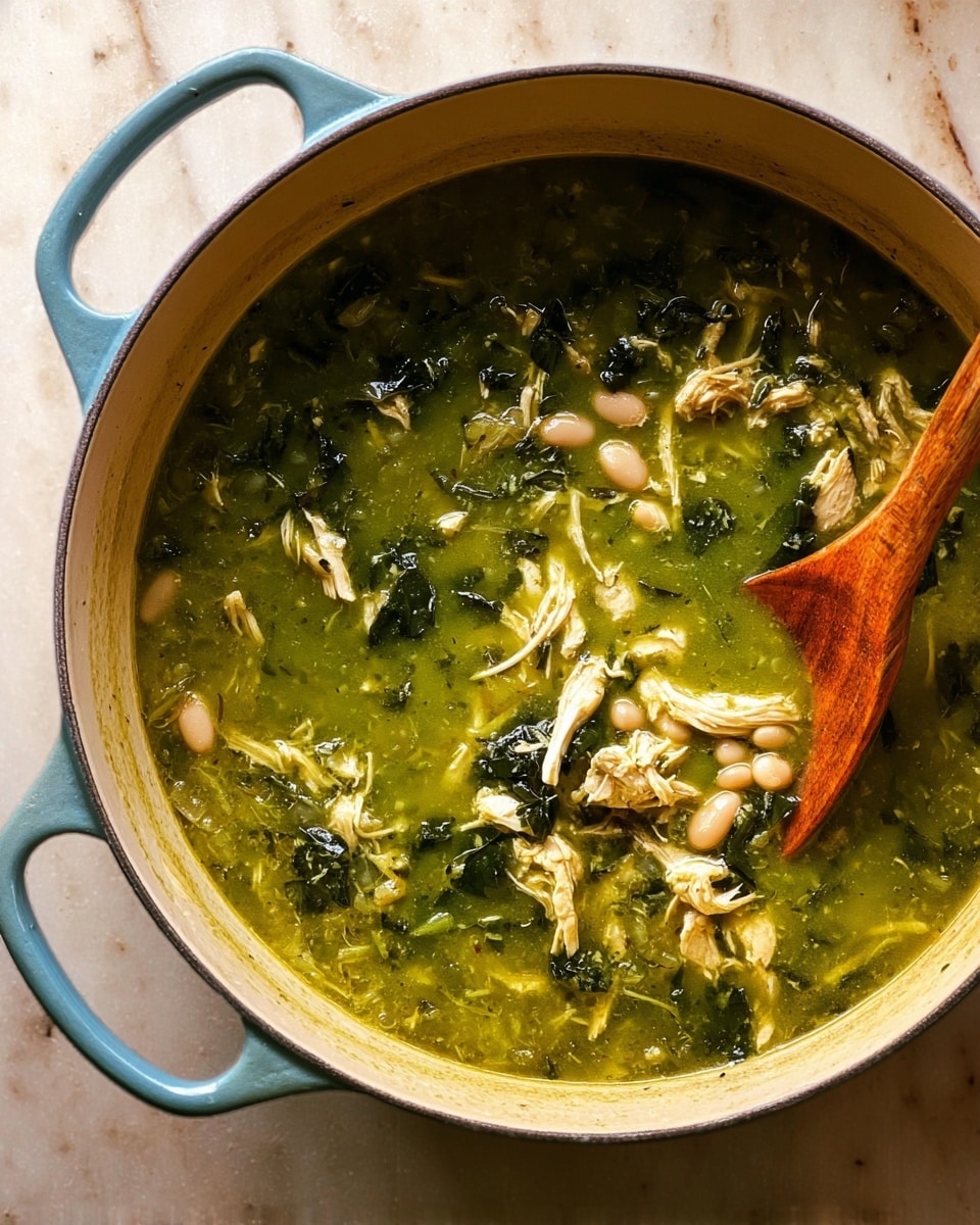 A large light blue pot filled with thick green soup showing visible shredded white pieces of chicken, small white beans, and dark green leafy bits. A wooden spoon rests inside the pot on the right side. The soup texture looks slightly chunky with a smooth base, and the scene is set on a white marbled surface. photo taken with an iphone --ar 4:5 --v 7