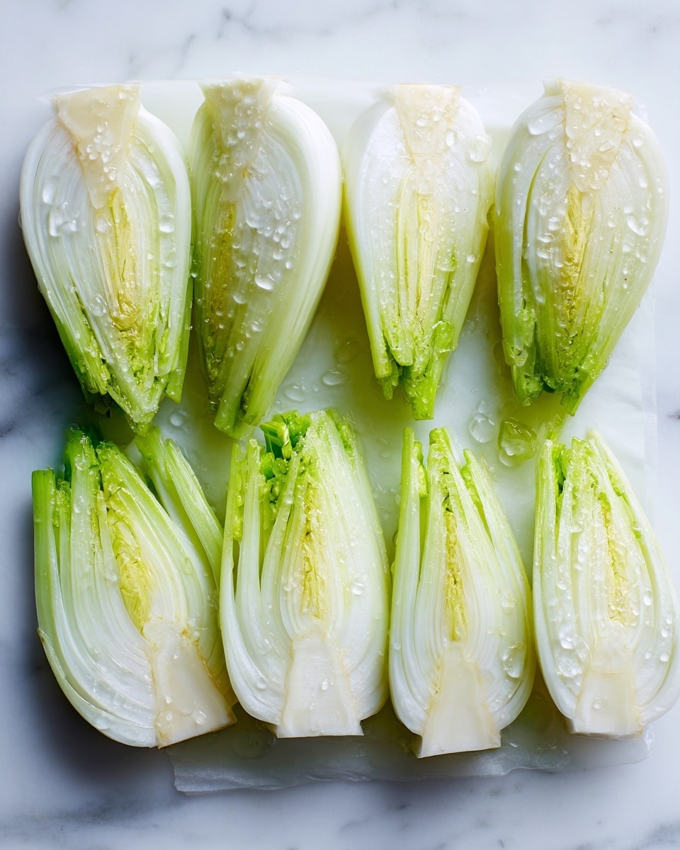 The image shows six pieces of fennel laid out in a row on a sheet of parchment paper placed on a white marbled surface. Each fennel piece is cut lengthwise, revealing layers of pale green and white with a slightly translucent, crisp texture. The outer layers are light green, and the inner layers are white with a smooth, moist look, some pieces displaying the stalk attached at the top. Light droplets of oil or moisture glisten softly on the fennel surfaces, adding a fresh and slightly shiny appearance. photo taken with an iphone --ar 4:5 --v 7