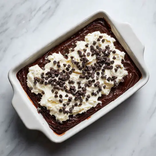 A white rectangular baking dish filled with a thick dark brown chocolate batter as the bottom layer, topped with uneven dollops of creamy white cheese mixture scattered across the surface. Small dark chocolate chips are sprinkled generously over both the chocolate batter and cheese dollops, adding texture and contrast. The dish sits on a white marbled surface, and the image shows a close-up view highlighting the rich texture and contrast between dark chocolate and white cheese. Photo taken with an iphone --ar 4:5 --v 7