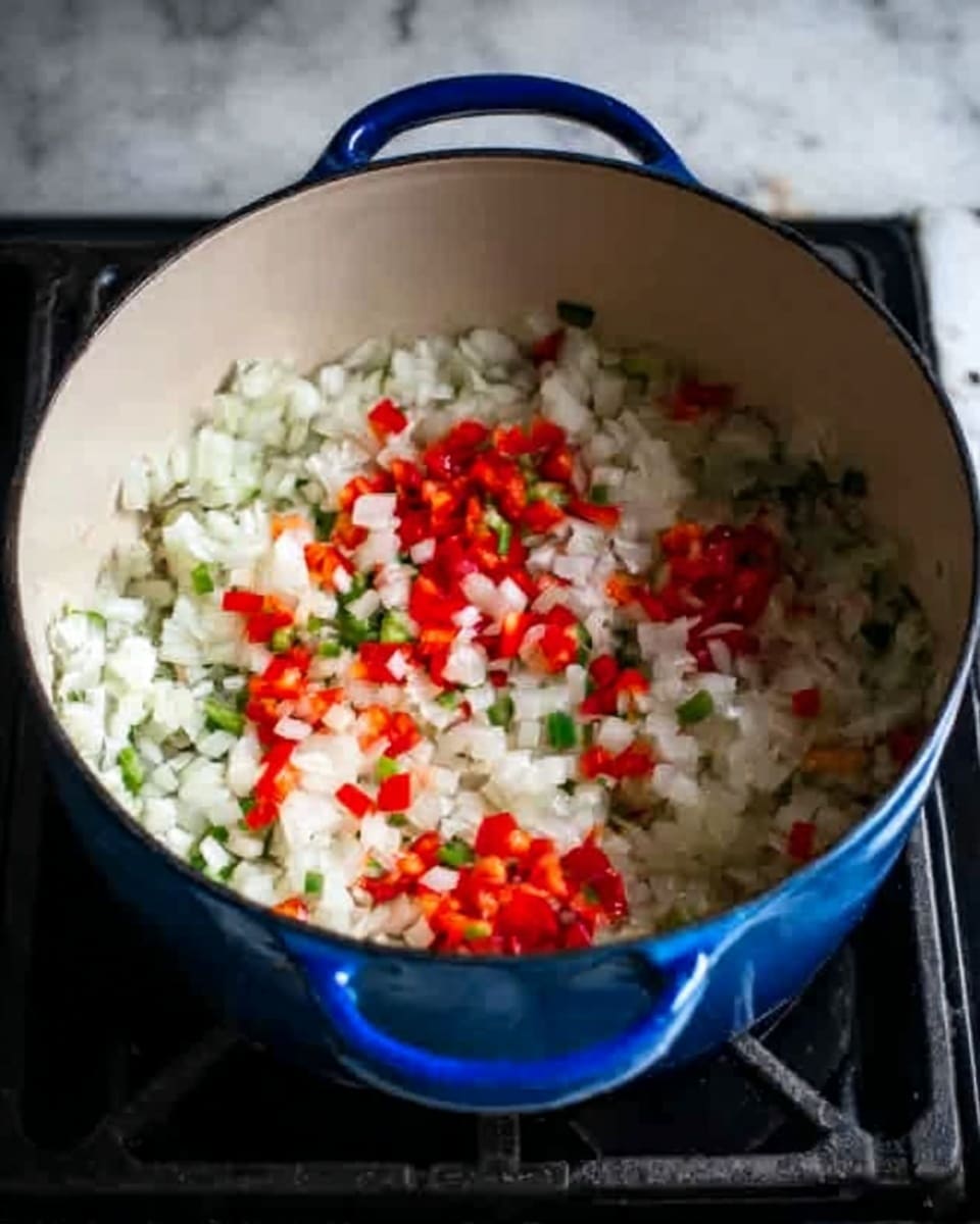 A large blue pot is shown from above, placed on a black stove with a white marbled surface beneath. Inside the pot, there are finely chopped white onions mixed with small pieces of red and green bell peppers. The onions cover most of the bottom layer, with the colorful peppers scattered evenly on top, creating a textured, fresh look. The lighting highlights the shiny, moist texture of the vegetables. photo taken with an iphone --ar 4:5 --v 7