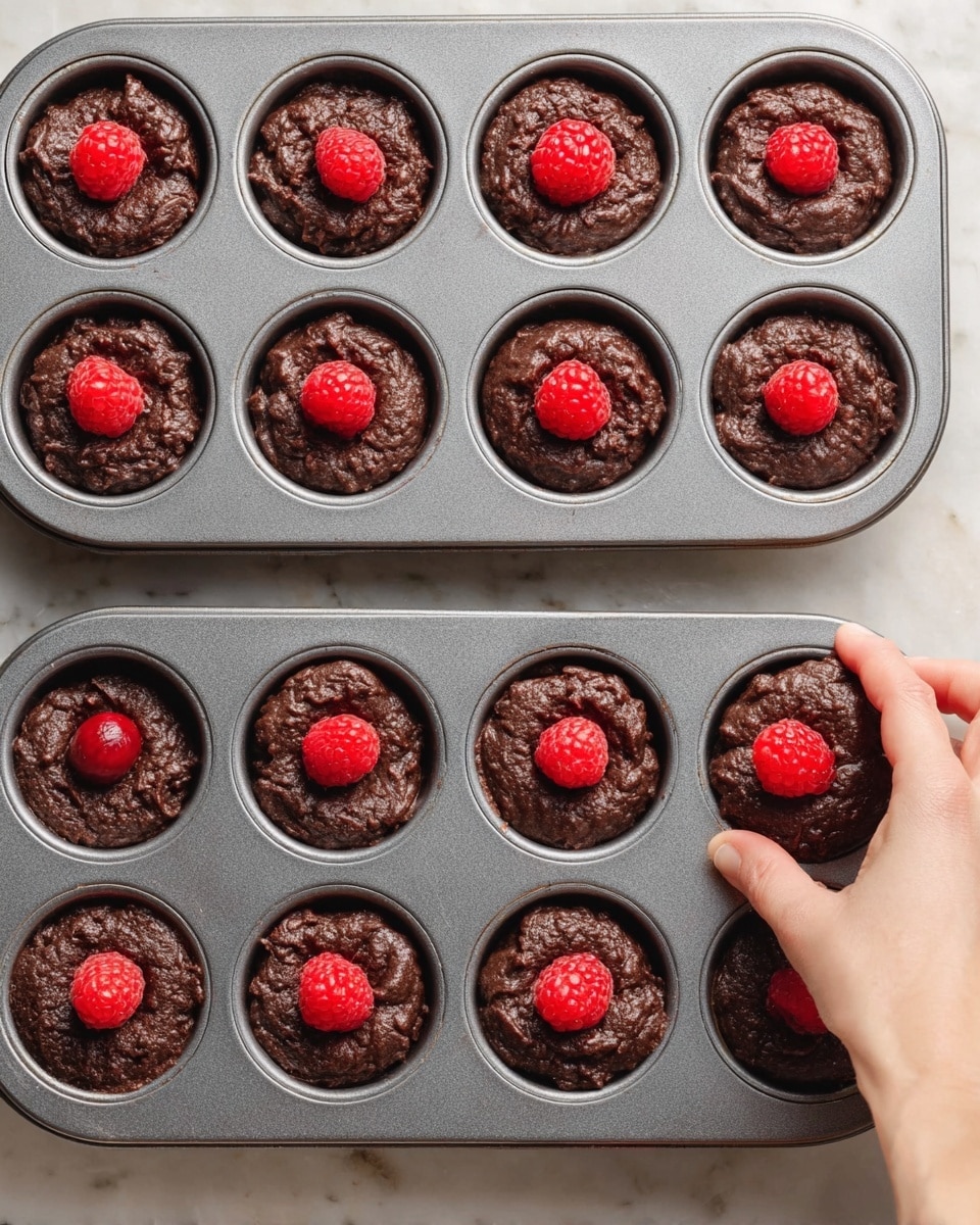 A clear glass bowl filled with bright red raspberries, each raspberry showing detailed small, bumpy texture and tiny seeds with hollow centers visible, the bowl placed on a white marbled surface. The raspberries are piled on top of each other, creating a full and fresh look with natural soft shadows. Photo taken with an iphone --ar 4:5 --v 7
