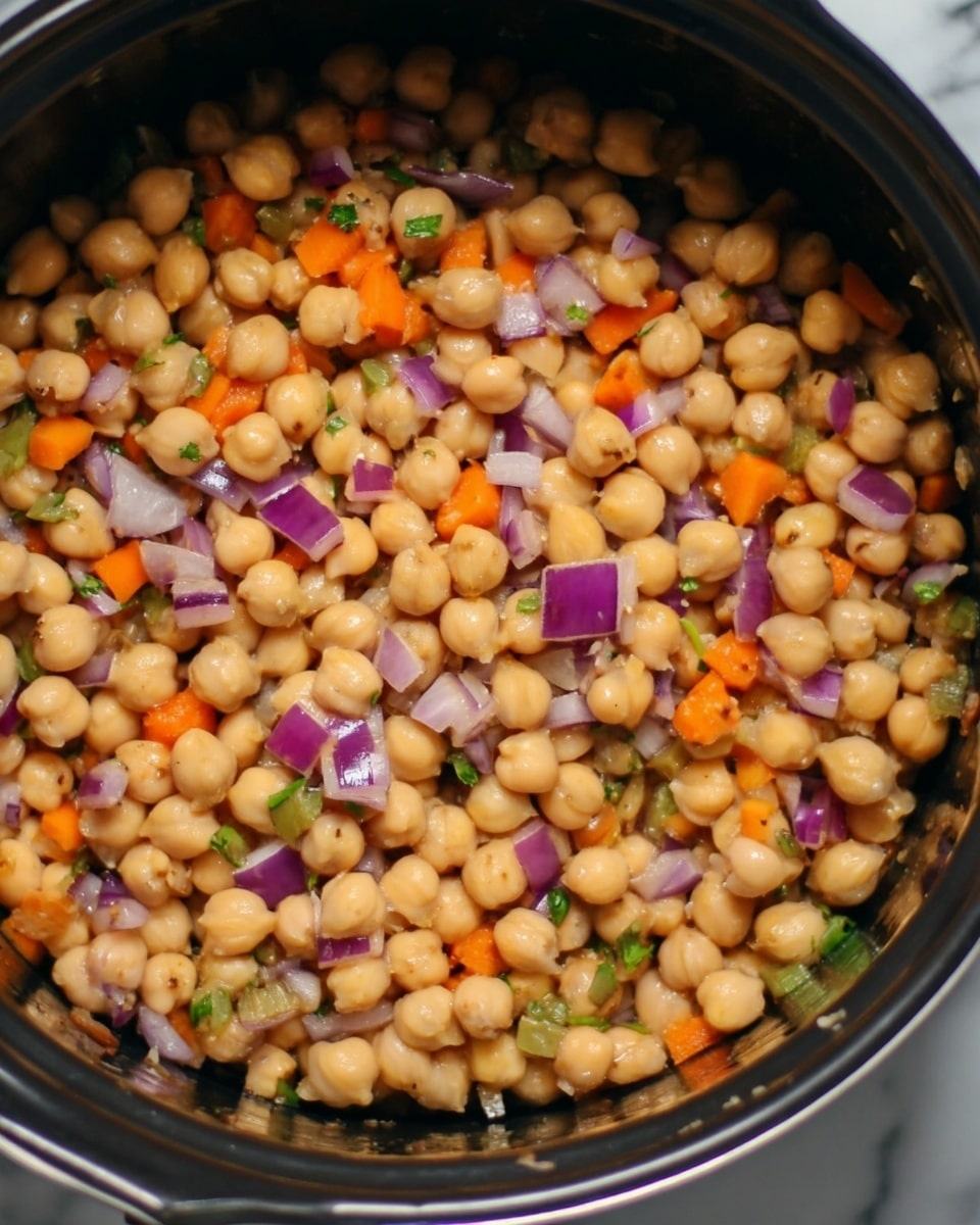 The image shows a close-up view of a black cooking pot filled with cooked chickpeas mixed with small pieces of orange carrots, purple onions, and green herbs. The chickpeas form the main layer, showcasing a soft and slightly shiny texture with a light tan color. Scattered evenly among the chickpeas are diced vegetables adding pops of bright color and contrast. The inside of the pot is dark, highlighting the colors of the ingredients. The background and surface around the pot have a white marbled texture. photo taken with an iphone --ar 4:5 --v 7