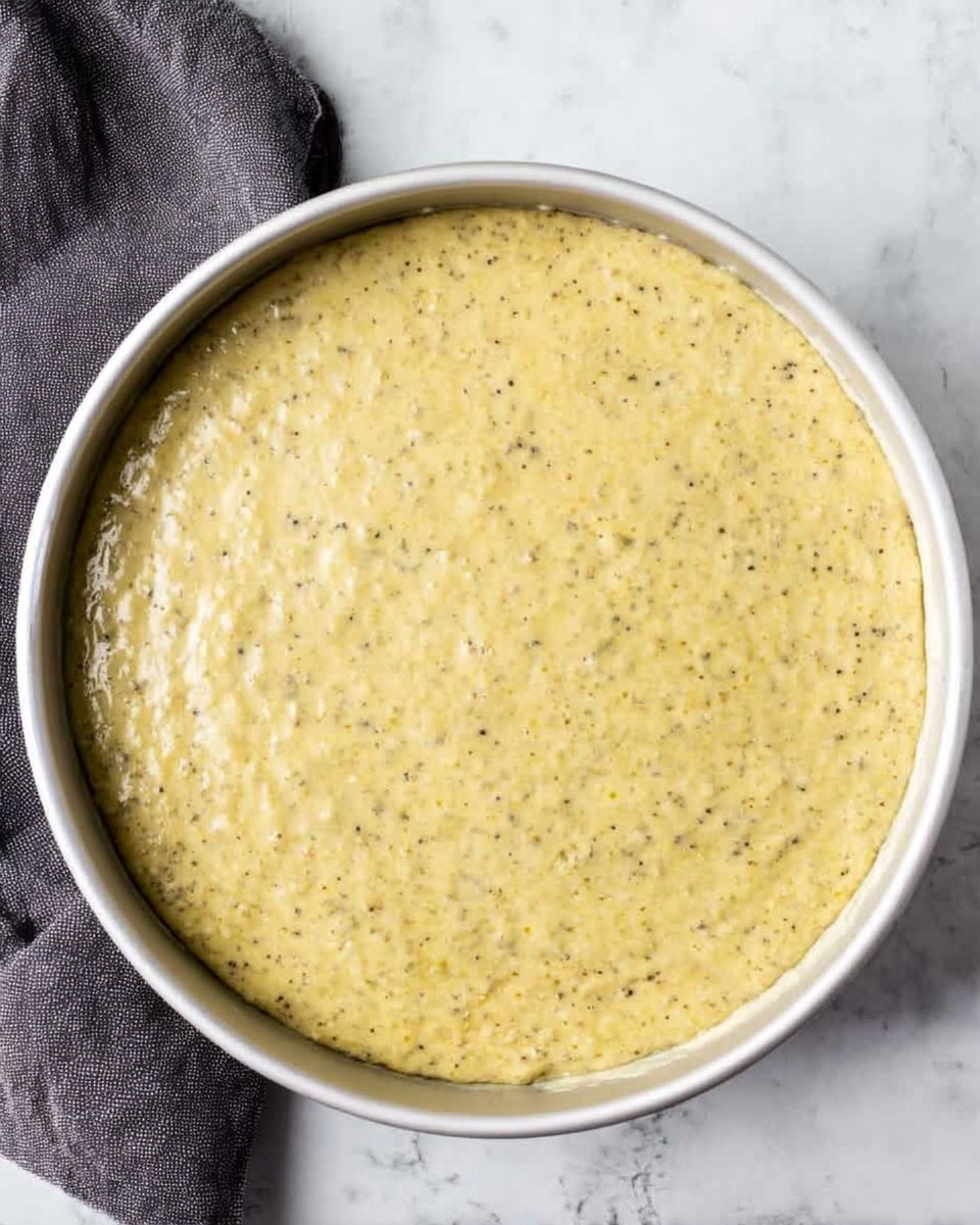 A slice of yellow-greenish cake with a soft, crumbly texture is placed on a white plate. The cake has a thin dusting of powdered sugar on top. On top of the slice, there is a dollop of white whipped cream with two bright red raspberries next to it. Around the slice, there are two more raspberries on the plate. In the background, more pieces of the same cake are stacked, slightly blurred. The plate sits on a white marbled surface. Photo taken with an iphone --ar 4:5 --v 7