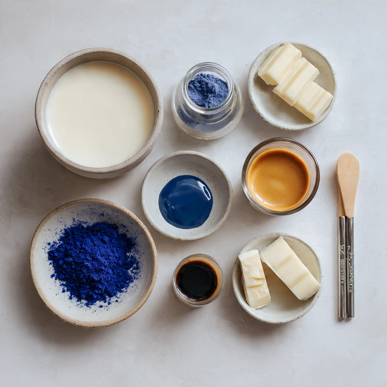 A transparent glass with white paint spots on its outside is placed on a white plate with colorful floral designs. A woman's hand is holding a small ladle with light cream liquid inside, pouring the liquid into the glass. In the background, there is a brown vase with delicate white flowers and a soft white cloth resting nearby. The setting is on a white marbled surface with some scattered white flakes, and the backdrop includes soft natural light and a dark blurred area. Photo taken with an iphone --ar 4:5 --v 7