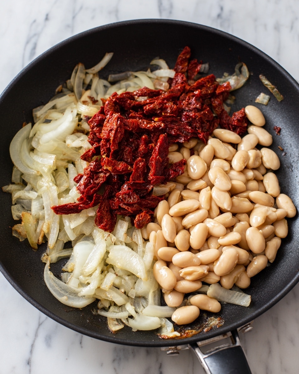 The image shows a close-up of a black frying pan with three main layers of ingredients. The first layer consists of translucent, sautéed onion slices spread unevenly around the edges of the pan, showing light browning. The second layer, placed on the right side of the pan, is a heap of small, smooth, pale beige beans with a soft, glossy texture. The third layer, situated near the center of the pan and extending a little to the left, is a mass of finely chopped, deep red sun-dried tomatoes with a slightly rough and moist appearance. The background is a white marbled surface. Photo taken with an iphone --ar 4:5 --v 7