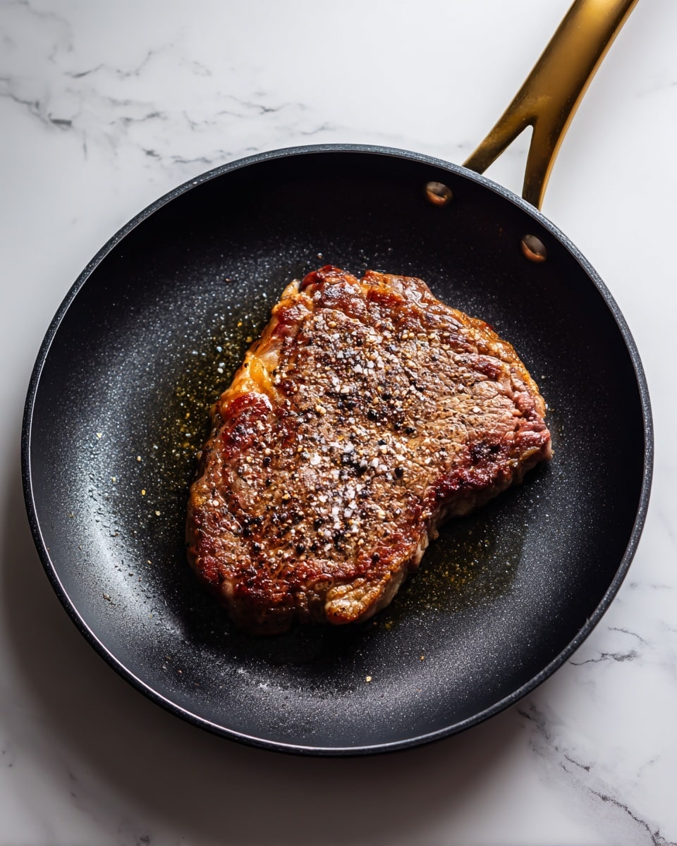 A white plate sits on a white marbled surface with a cooked flat piece of brown beef in the center. The meat is dark brown with a slightly shiny texture and small bits of red sauce on top. Around the beef are large chunks of golden potatoes and bright orange carrot pieces, all cooked and slightly glossy. Small green herb leaves are scattered over the meat and vegetables. A blue and white striped cloth is partly visible at the edge of the surface near the plate. photo taken with an iphone --ar 4:5 --v 7