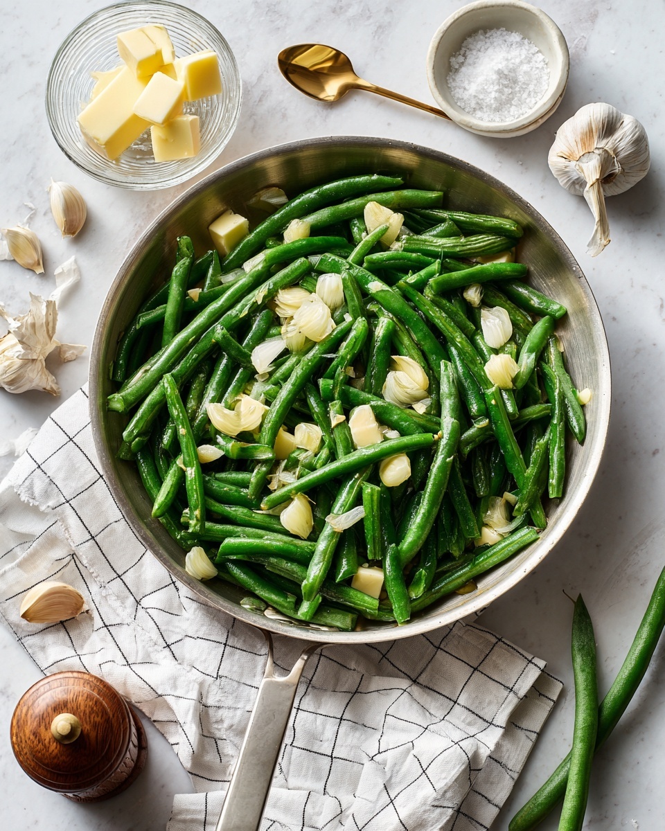 A silver pan filled with bright green whole green beans forms the base layer, topped with scattered slices of light beige garlic cloves and small chunks of pale yellow butter. Around the pan on a white marbled surface, there are two green beans off to the right, a small clear glass bowl with three pale yellow butter pieces, two garlic cloves, a white salt container with salt and a small gold spoon, and a brown wooden pepper grinder. A white cloth with black grid lines is laid out under the pan's handle. The overall look is fresh and clean with natural light, photo taken with an iphone --ar 4:5 --v 7