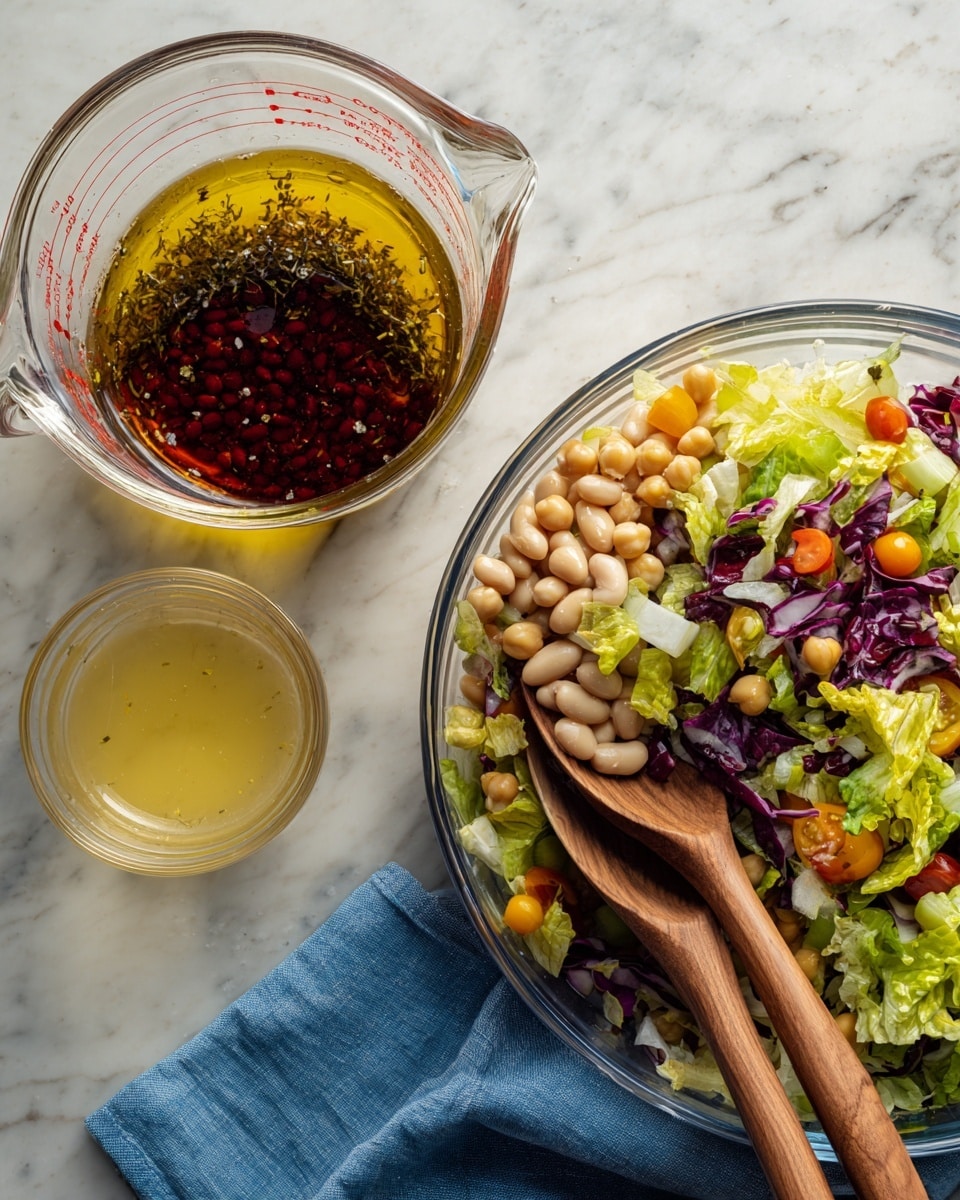 On the left side, there is a clear glass measuring cup with four distinct liquid layers: a bottom layer with small white beans, a thick dark red layer above it, a thin black herb layer next, and a top golden yellow olive oil layer with some herbs floating inside. On the right side, there is a large clear glass bowl filled with a colorful mixed salad, showing several layers of ingredients from the top: bright green lettuce, purple radicchio, small orange cherry tomatoes, yellow chickpeas, and pieces of celery, all mixed evenly. Two wooden spoons are placed inside the bowl, and a small clear glass container with light yellow dressing is next to it on a white marbled surface with a blue cloth nearby. Photo taken with an iphone --ar 4:5 --v 7