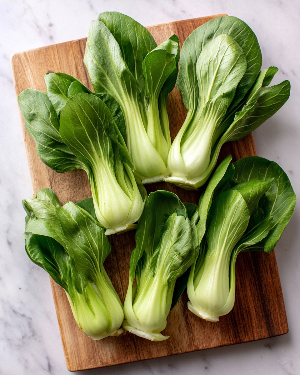 The image shows several halves of fresh bok choy arranged on a wooden cutting board. Each piece has bright green leaves on top, which are broad and leafy with a slightly glossy texture. The stems beneath are thick, pale green, and firm, with a smooth surface. The cutting board is placed on a white marbled surface, creating a clean and simple background. The bok choy halves are spaced unevenly, showing the contrast between the leafy tops and the solid stems clearly. Photo taken with an iphone --ar 4:5 --v 7
