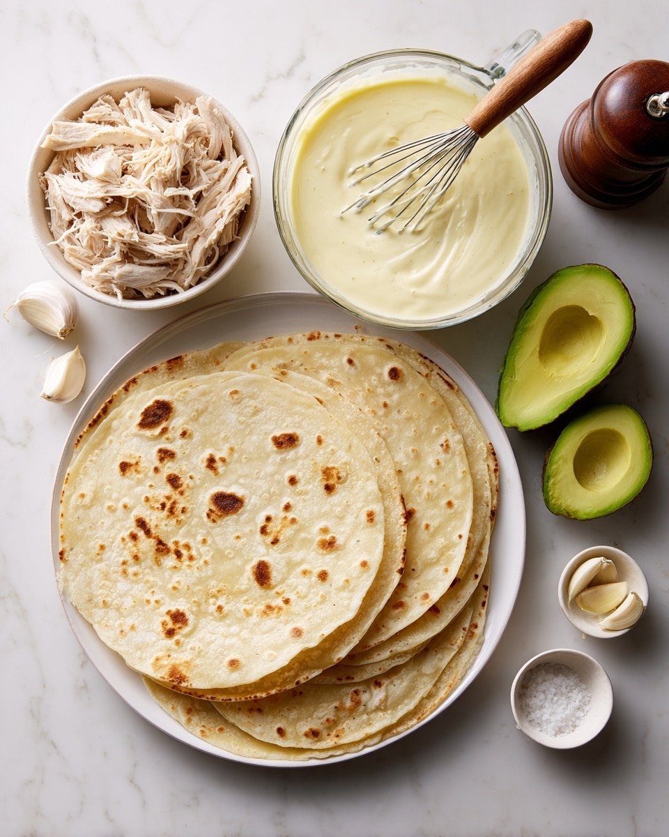 The image shows a white plate at the bottom with several round, light beige tortillas stacked neatly, each having slight brown spots. Above the plate is a clear glass measuring cup filled with thick, creamy light yellow sauce with a smooth texture, with a whisk that has a wooden handle resting inside. To the top left, there is a white bowl full of shredded pale beige chicken with a fibrous texture. To the right, two halves of a bright green avocado with a creamy texture are placed on a white marbled surface. Small white bowls contain garlic cloves and a dark wooden pepper grinder is positioned toward the bottom right. The photo is taken with an iphone --ar 4:5 --v 7