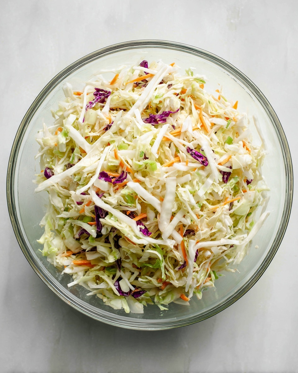 A clear glass bowl filled with shredded cabbage salad sits on a white marbled surface. The salad has three main layers: thin white cabbage strips dominate the top and middle layers, mixed with light green cabbage pieces and pale slices of celery. There are also small bits of orange carrot and purple cabbage scattered throughout, adding color contrast and texture. The shredded ingredients are loosely mixed, showing some pieces lying flat while others stand up slightly. The bowl’s transparency reveals the mix from different angles, and the whole scene is lit to show fresh, natural colors. photo taken with an iphone --ar 4:5 --v 7