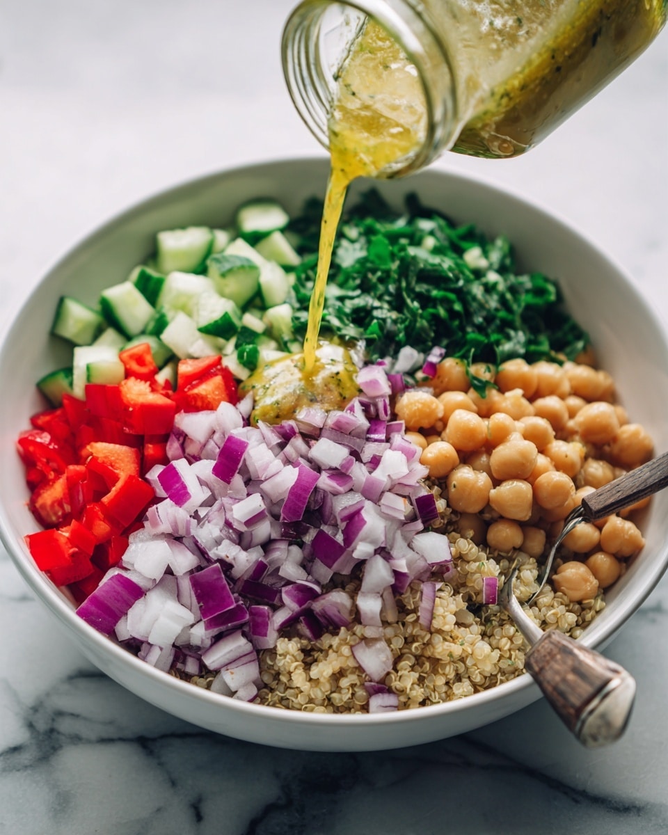A white bowl filled with five layers of fresh chopped ingredients sitting on a white marbled surface. The first layer includes small round chickpeas and quinoa forming the base, visible at the bottom edges. On top of that, a pile of finely chopped purple onions sits on the right with white and purple square pieces. Beside the onions, there are small red bell pepper cubes. Next to that is a pile of finely chopped dark green leafy herbs. At the top left, there are diced light green cucumber pieces. A yellow dressing is being poured from a clear glass jar into the center of the bowl, flowing over the green herbs and cucumbers. A silver spoon with a wooden handle rests inside the bowl on the right edge. Photo taken with an iphone --ar 4:5 --v 7