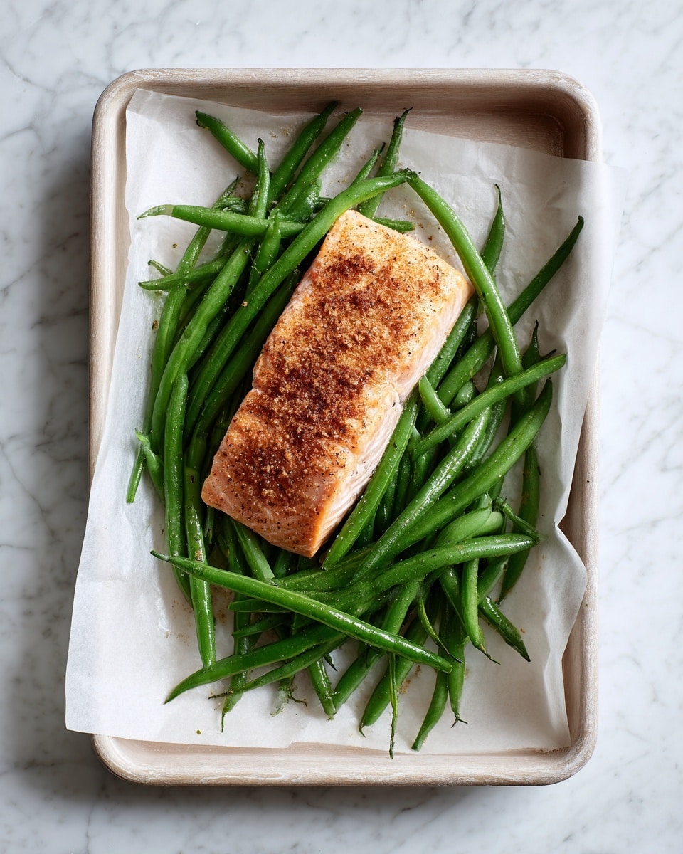 The image shows a single rectangular piece of salmon with a light brown seasoning crust on top, positioned at the upper right side of a white parchment-lined tray. Below and slightly to the left of the salmon, there is a loosely spread pile of green beans, bright green and fresh, some overlapping each other. The tray itself rests on a white marbled surface, with the overall arrangement centered and simple without any other food items. Photo taken with an iphone --ar 4:5 --v 7