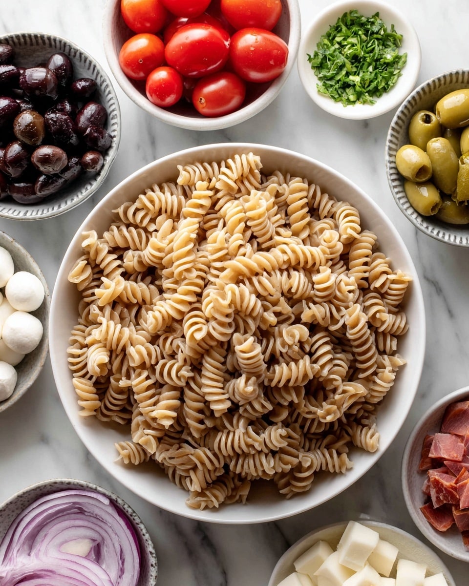 A large white bowl filled with light brown cooked spiral pasta sits in the center on a white marbled surface. Around it are smaller white bowls: one with bright red halved cherry tomatoes, one with dark black olives, one with light green sliced pepperoncini, and a small white bowl with chopped green herbs at the top center. There are also two gray patterned bowls, one with small white mozzarella balls and one with small cubes of reddish cured meat. Thinly sliced light purple onions are visible at the bottom left corner. Everything is arranged neatly and clearly for making a pasta salad photo taken with an iphone --ar 4:5 --v 7