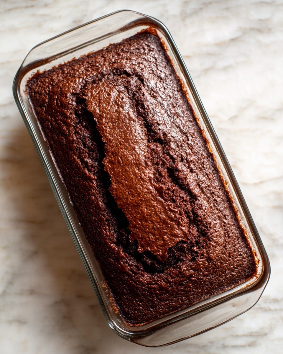 A rectangular chocolate cake loaf sits on a wooden surface with thick, shiny chocolate frosting spread unevenly on top and along the sides. The cake has been sliced into four pieces, showing a dense, dark, moist chocolate interior with the frosting generously layered between each slice. The frosting has a smooth yet slightly textured appearance, creating glossy ridges and swirls. A silver knife with some frosting on the blade rests to the left of the cake. The background is softly blurred with warm tones. photo taken with an iphone --ar 4:5 --v 7