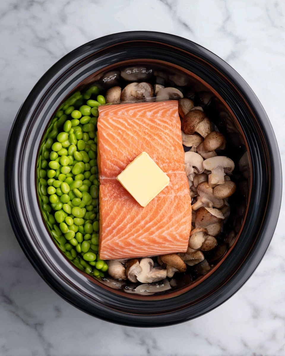 Inside a black rice cooker, there is one thick piece of fresh orange salmon on top. The salmon has a smooth texture with visible light pink lines, and on top of it sits a square pat of pale yellow butter. Around the salmon are two layers: bright green edamame beans on one side and light brown and beige mushrooms on the other side. The inside of the cooker has white measurement marks, and the background shows a white marbled surface. photo taken with an iphone --ar 4:5 --v 7