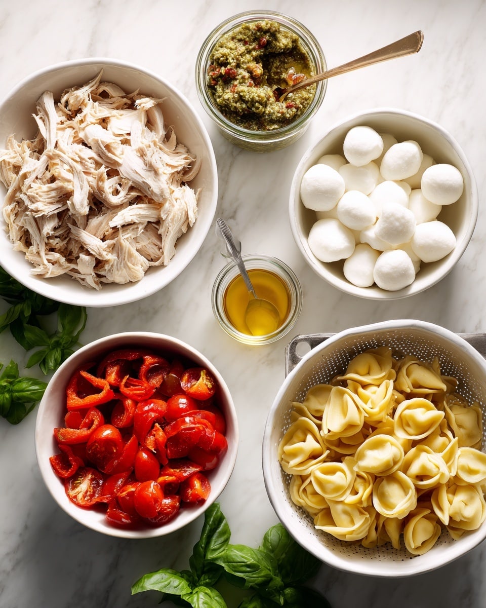 The image shows several white bowls and a colander placed on a white marbled surface. On the left, there is a white bowl filled with shredded light-colored cooked chicken. Next to it, a white bowl contains roasted red pepper pieces that are shiny and soft. Below that, another white bowl holds halved red cherry tomatoes with visible seeds inside. Towards the center, a small white cup contains a small amount of golden olive oil. A bunch of fresh green basil leaves sits in front of the bowls. To the right, there is a white bowl filled with small white mozzarella balls, and a small jar above it contains green pesto sauce with a golden spoon inside. Finally, a white colander on the right side is full of uncooked yellow tortellini pasta with a folded and slightly twisted shape. Photo taken with an iphone --ar 4:5 --v 7