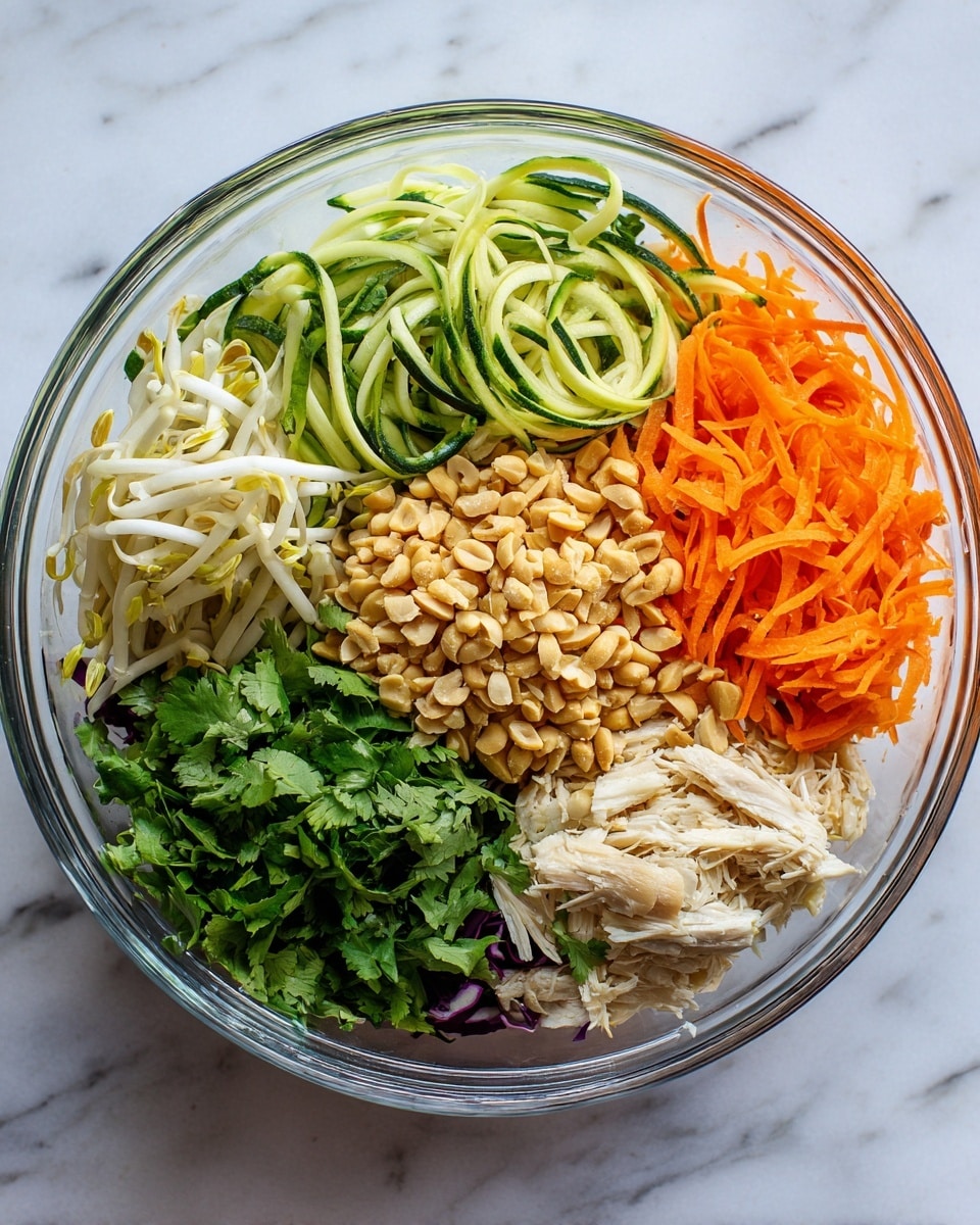 A clear glass bowl on a white marbled surface holds a colorful salad arranged in six separate layers. Starting from the top right moving clockwise, there is a pile of shredded light orange carrots, followed by light green zucchini spirals. Next to that is a small section of white bean sprouts. Below the sprouts is a bunch of fresh green cilantro leaves. Above the cilantro is a mound of finely shredded purple cabbage. In the center of the bowl is a cluster of crushed light brown peanuts, surrounded by shredded white cooked chicken. Photo taken with an iphone --ar 4:5 --v 7