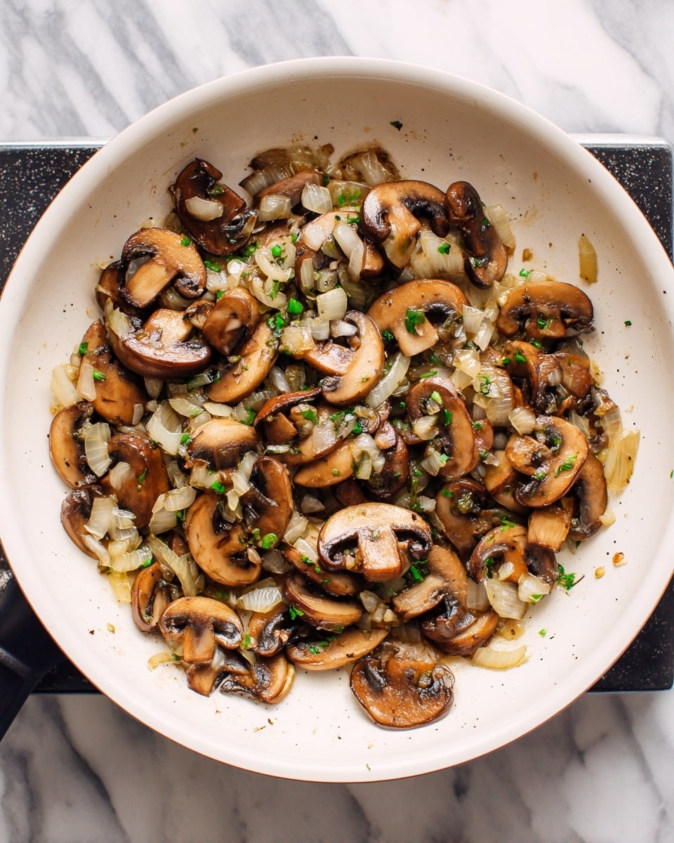 A white pan filled with cooked sliced mushrooms and small chopped onions, both browned and slightly soft. The mushrooms are medium brown with darker edges, spread evenly across the pan’s surface. The onions are translucent with a light golden tint, mixed throughout the mushrooms. The pan is placed on a black stove burner, and the background has a smooth white marbled texture. photo taken with an iphone --ar 4:5 --v 7