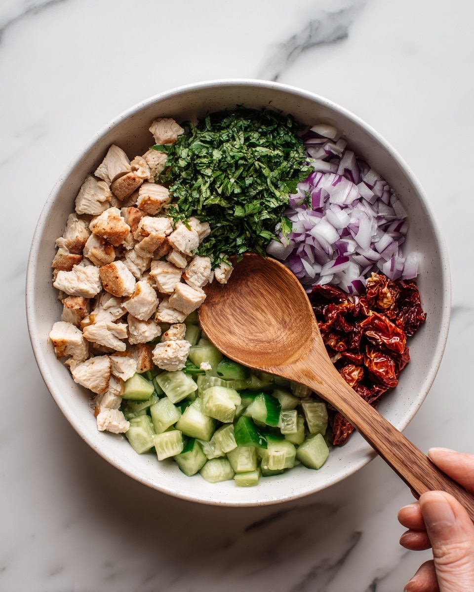 In a white bowl on a white marbled surface, there are five main layers arranged separately. The largest section contains small cubes of light brown cooked chicken placed on the left side. Next to it, at the top, is a pile of finely chopped dark green herbs. To the right of the herbs, there is a small section of finely chopped light purple onion. Below the onion, there are sun-dried tomatoes with a deep red color and slightly wrinkled texture. At the bottom right, there are bright green diced cucumbers. A wooden spoon with a smooth texture rests inside the bowl, its handle extending out from the left side, and a woman's hand lightly holds the spoon. Photo taken with an iphone --ar 4:5 --v 7