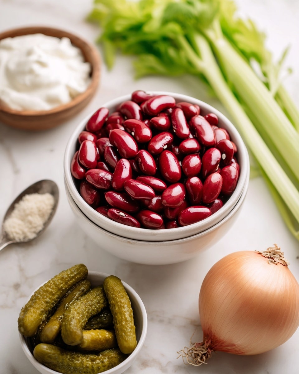The image shows a white bowl full of shiny red kidney beans in the center. To the right of the bowl, there is a whole light brown onion and a bunch of fresh green celery with leaves extending upwards. Below the kidney beans, there is a white bowl filled with small green pickles. On the left side, a silver spoon with a light beige powder rests on the white marbled surface, and behind it, a small wooden bowl holds a white creamy substance. The background is bright and soft, with a white marbled surface below everything. Photo taken with an iphone --ar 4:5 --v 7