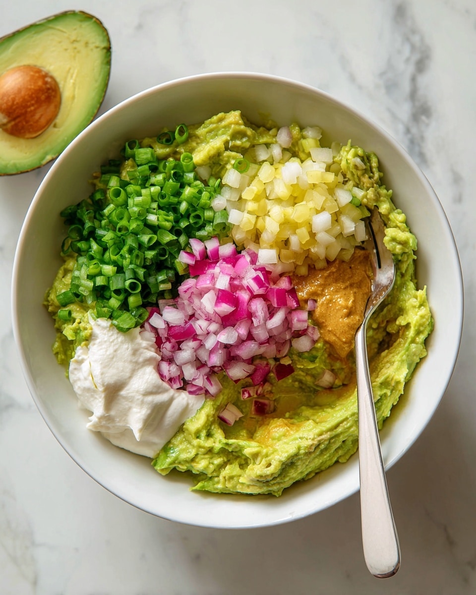 A white bowl filled with mashed avocado forming the base layer, light green and creamy in texture. On top, there are five distinct layers arranged closely: finely chopped bright green scallions on the upper left, pale yellow diced pickles on the upper right, a small heap of finely chopped red onions with white and pink tones in the center, a dollop of creamy white sour cream on the lower left, and a light brown mustard-like sauce on the lower right. A white-handled fork rests inside the bowl on the right side, partially covering the avocado. The bowl sits on a white marbled surface with a halved avocado placed nearby. photo taken with an iphone --ar 4:5 --v 7