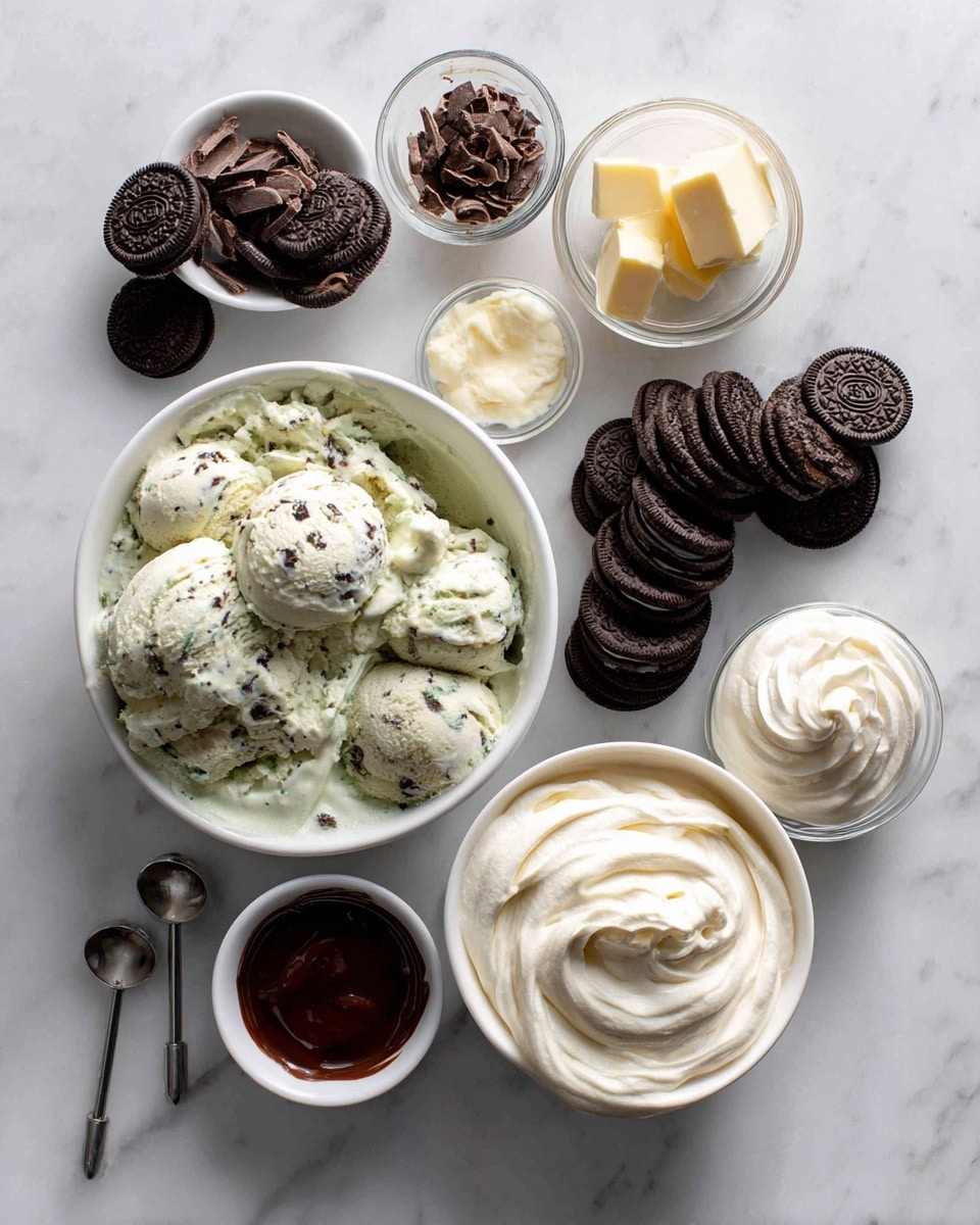 The image shows a slice of a layered dessert on a white plate with another white plate underneath, set on a white marbled surface. The dessert has a dark chocolate crumb base, a thick layer of light green creamy filling with specks of dark cookie pieces, and a topping of white whipped cream swirls decorated with small mint chocolate pieces and crumbled cookie bits. Thin streams of dark chocolate sauce drizzle down the sides. In the background, there is a blurred second dessert and a white cup. A cloth with gray and white stripes is partially visible in the lower part of the image. Photo taken with an iphone --ar 4:5 --v 7