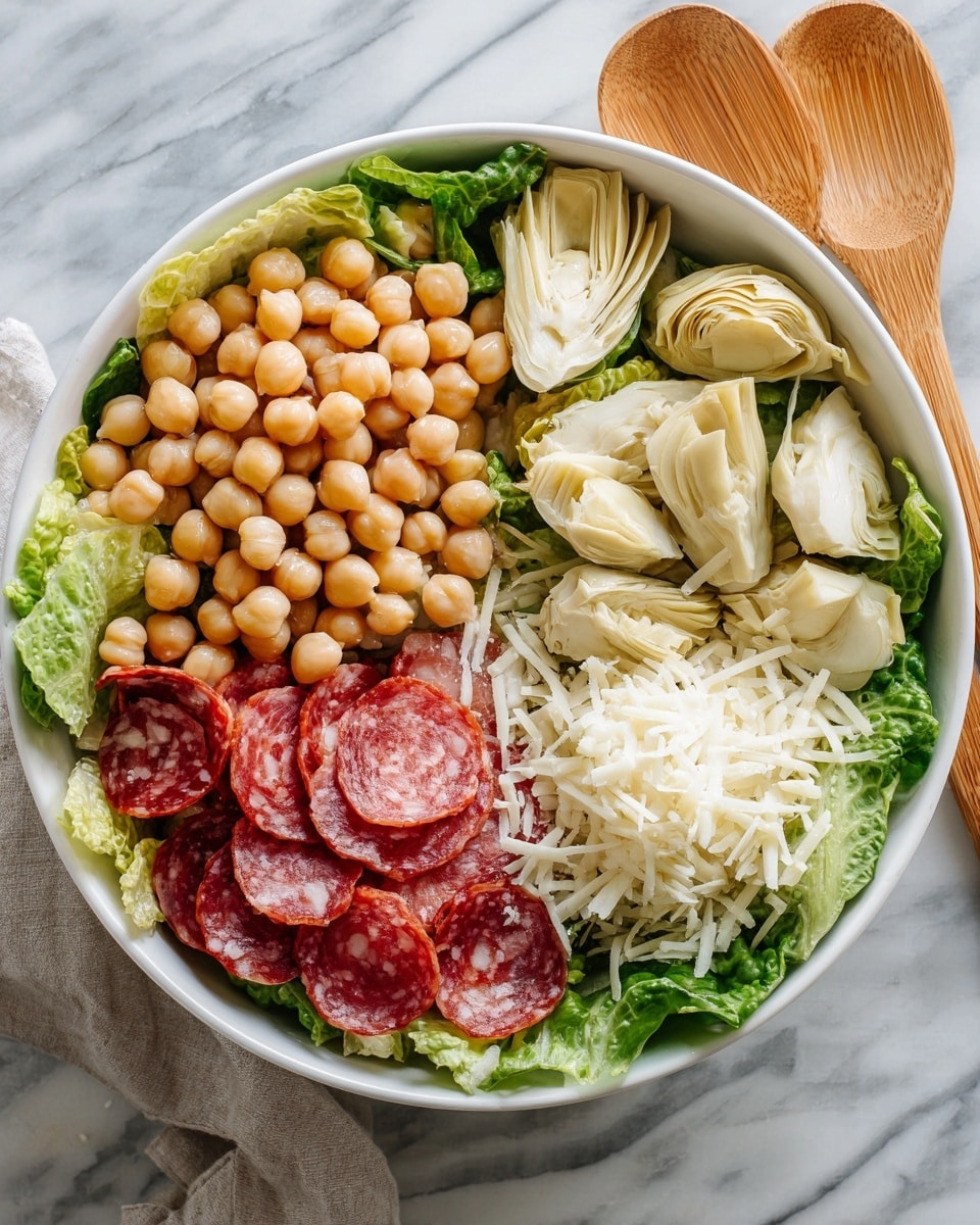 A white bowl is filled with a salad arranged in four sections over a base of green leafy lettuce. The top left section has a pile of round, beige chickpeas. The top right section holds soft, pale beige artichoke quarter pieces. The bottom right section contains a mound of white shredded cheese. The bottom left section has thin slices of red salami with white fat marbling. The bowl is set on a white marbled surface, and two wooden salad serving spoons are placed beside it. Photo taken with an iphone --ar 4:5 --v 7